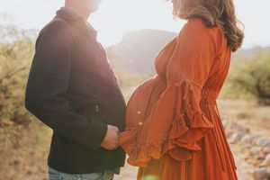 A couple embraces in a desert landscape at sunset with mountains in the background.