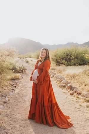A flowing rust-colored dress creates movement against a desert trail backdrop.