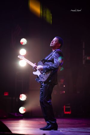 Male guitarist performing solo on stage under purple and white spotlights.