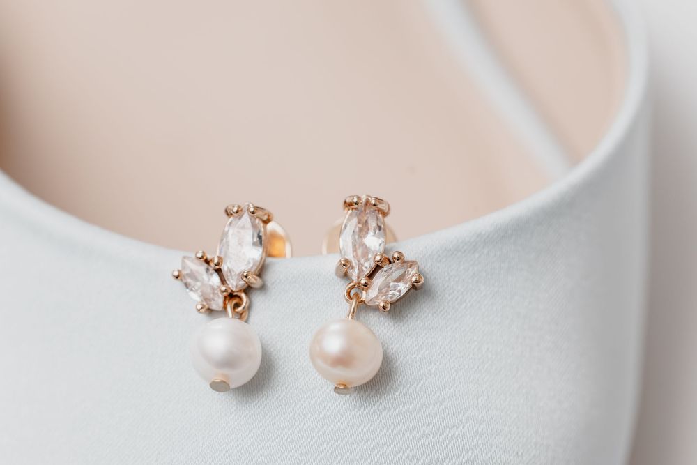 Gold drop earrings featuring crystal marquise stones and freshwater pearl pendants displayed on a white bridal shoe.