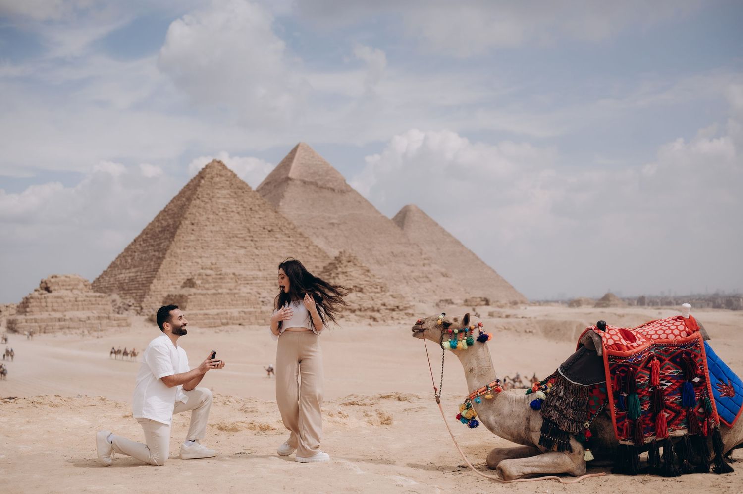 Romantic proposal scene in front of the Egyptian pyramids with a camel in the background.