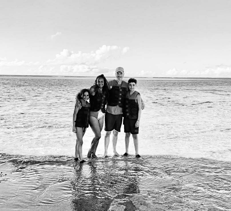 A group of people standing together in shallow ocean water on a sunny day with clouds in the background.