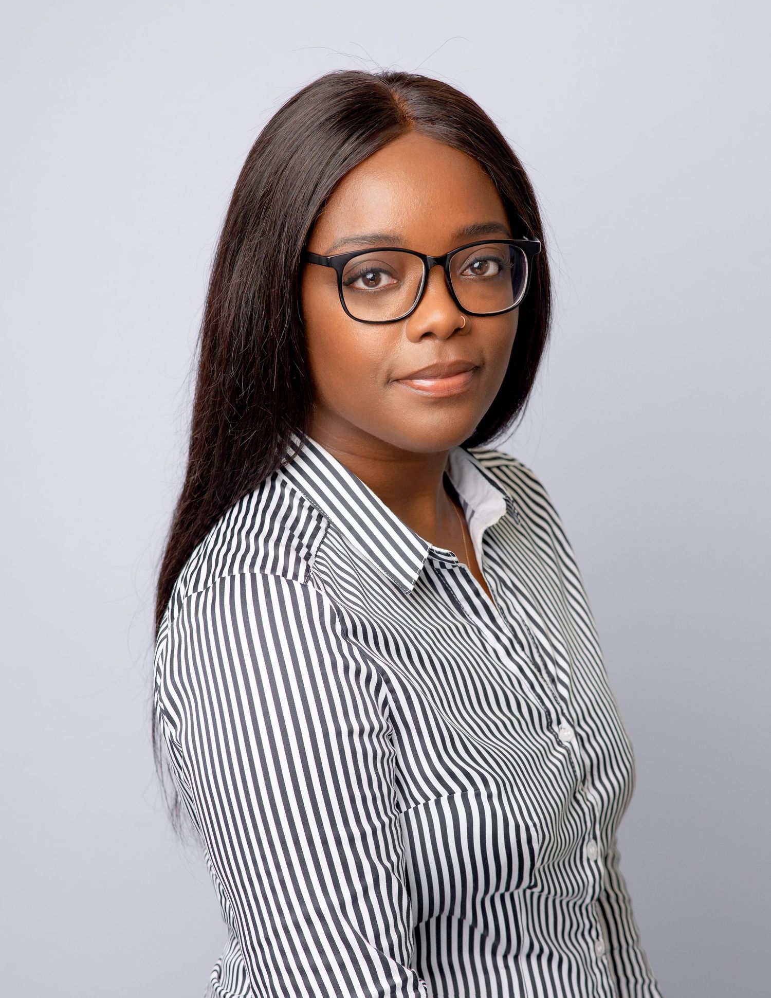 Professional portrait of someone wearing glasses and a black and white striped button-up shirt against a light gray background.
