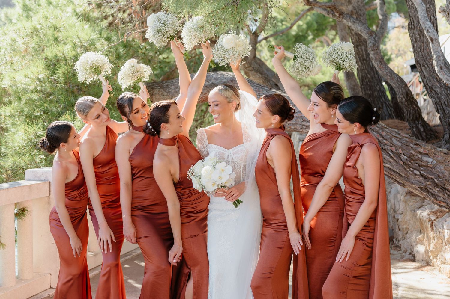 Wedding party in terracotta-colored dresses posing outdoors under pine trees.