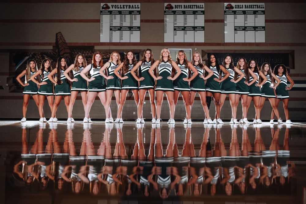 Dance team in matching uniforms poses on reflective floor creating mirror image effect in indoor venue.