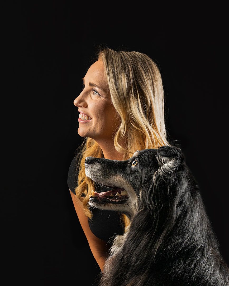 A profile portrait of a person with their black dog against a dark background.