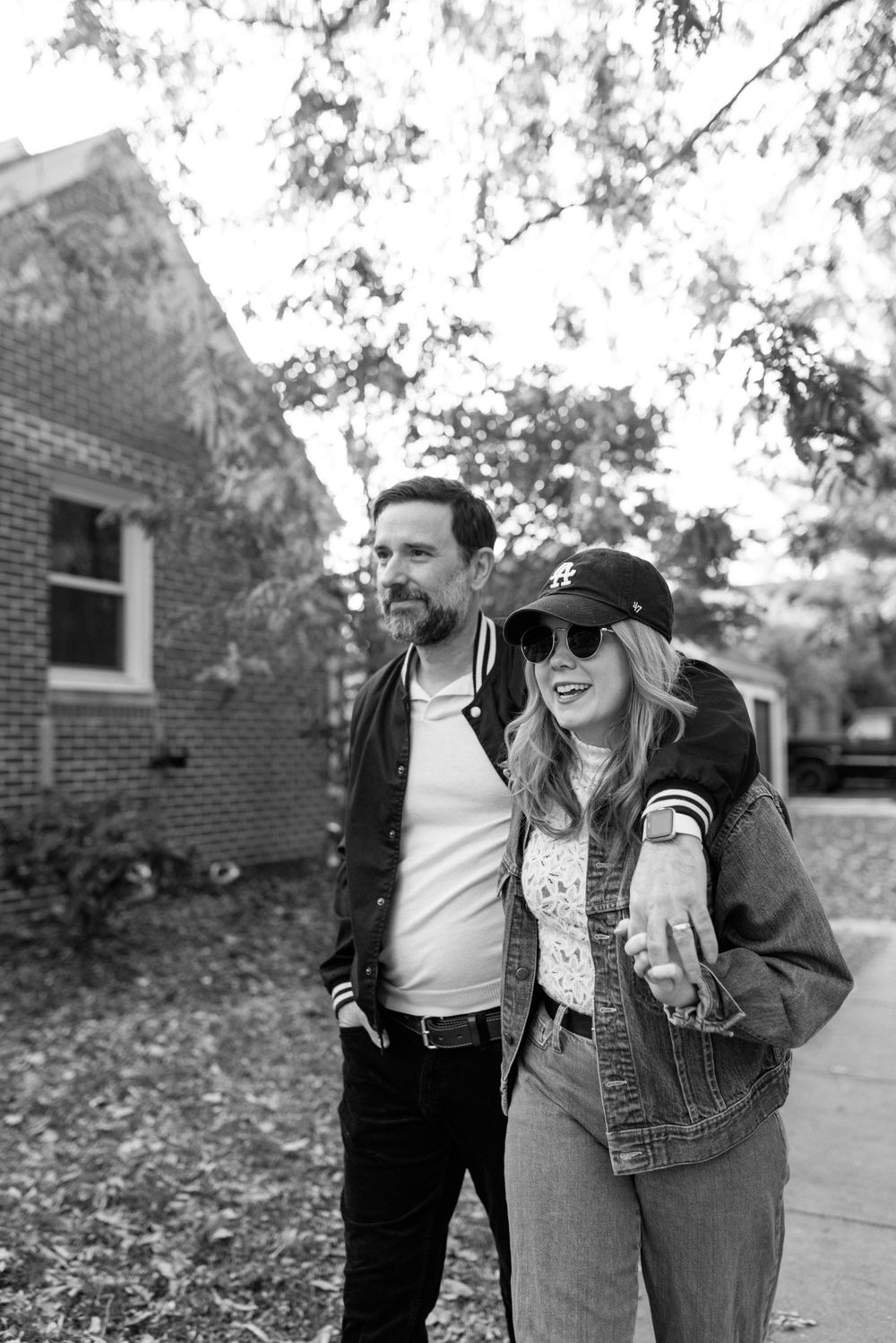 A couple in casual denim and leather attire smiling while walking together on a sidewalk during autumn.