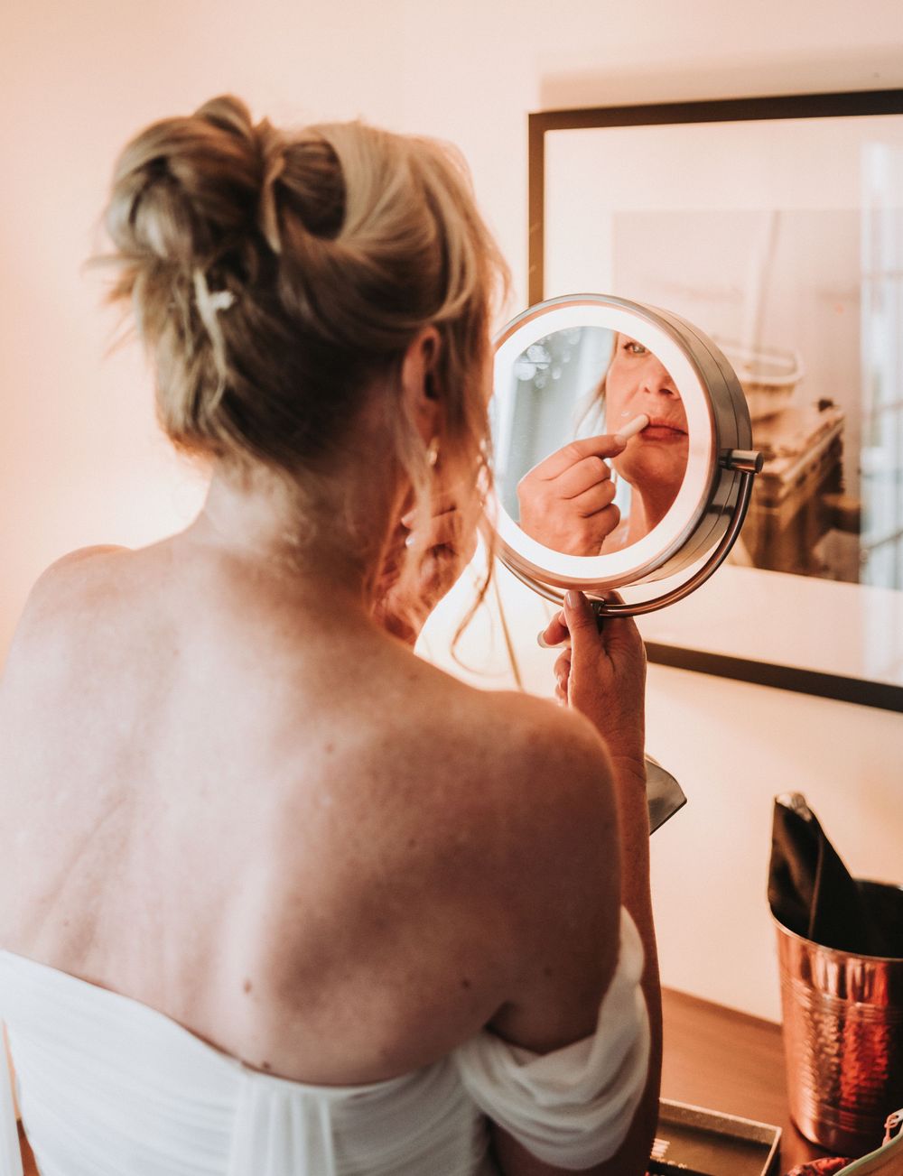 A bride gets ready for the ceremony using an illuminated makeup mirror while getting ready, with a soft warm-toned aesthetic.