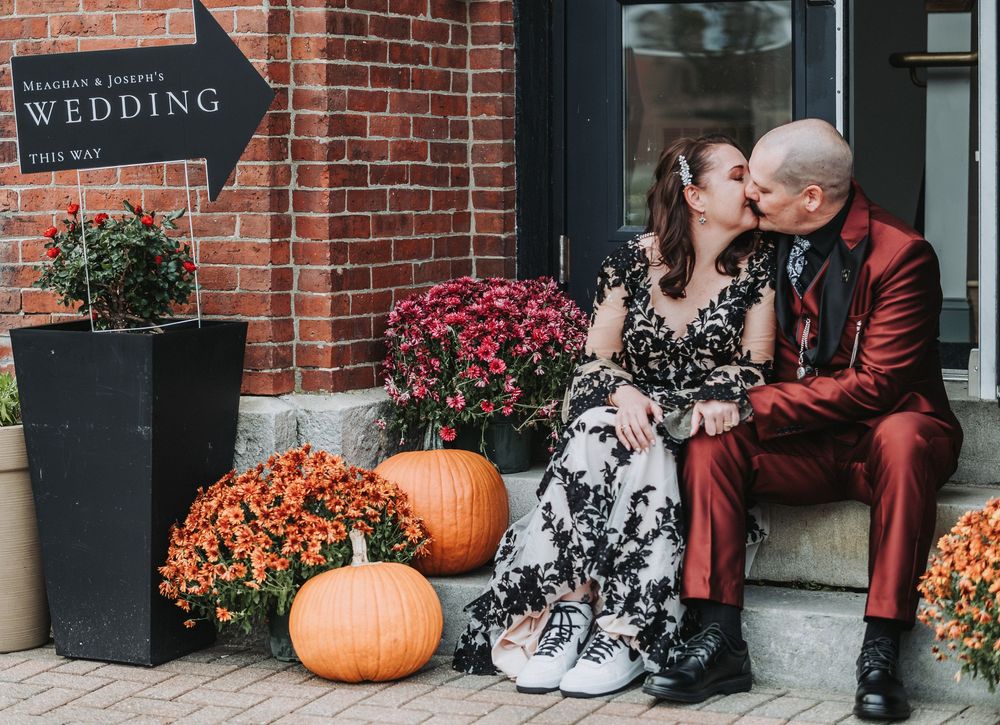 A couple sits on brick steps decorated with autumn pumpkins and flowers after their wedding at Lemont Hall in Brunswick, Maine.