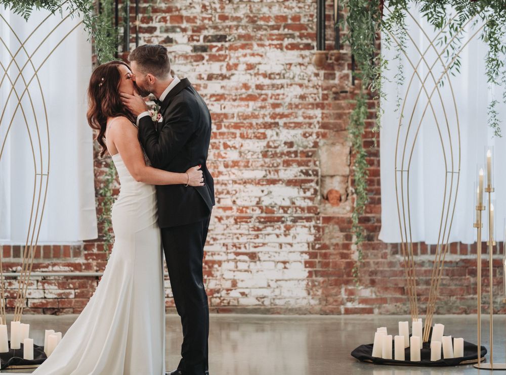 A romantic wedding moment with candles and greenery against a rustic exposed brick wall at an indoor venue.