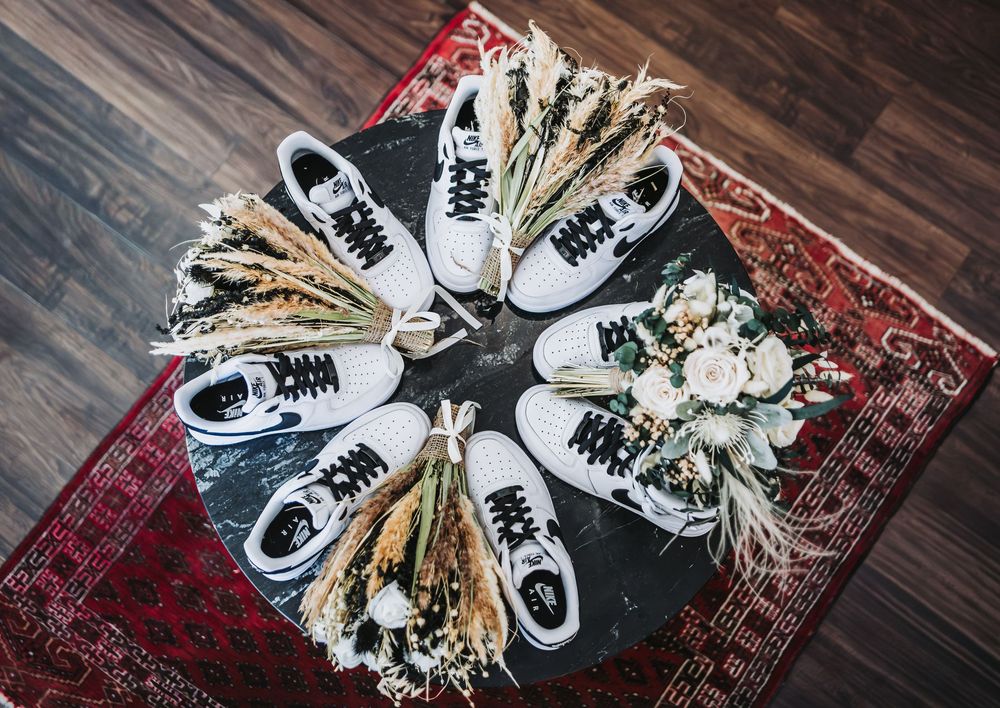 Wedding shoes and dried floral bouquet arranged on a dark wooden floor with a vintage red rug.
