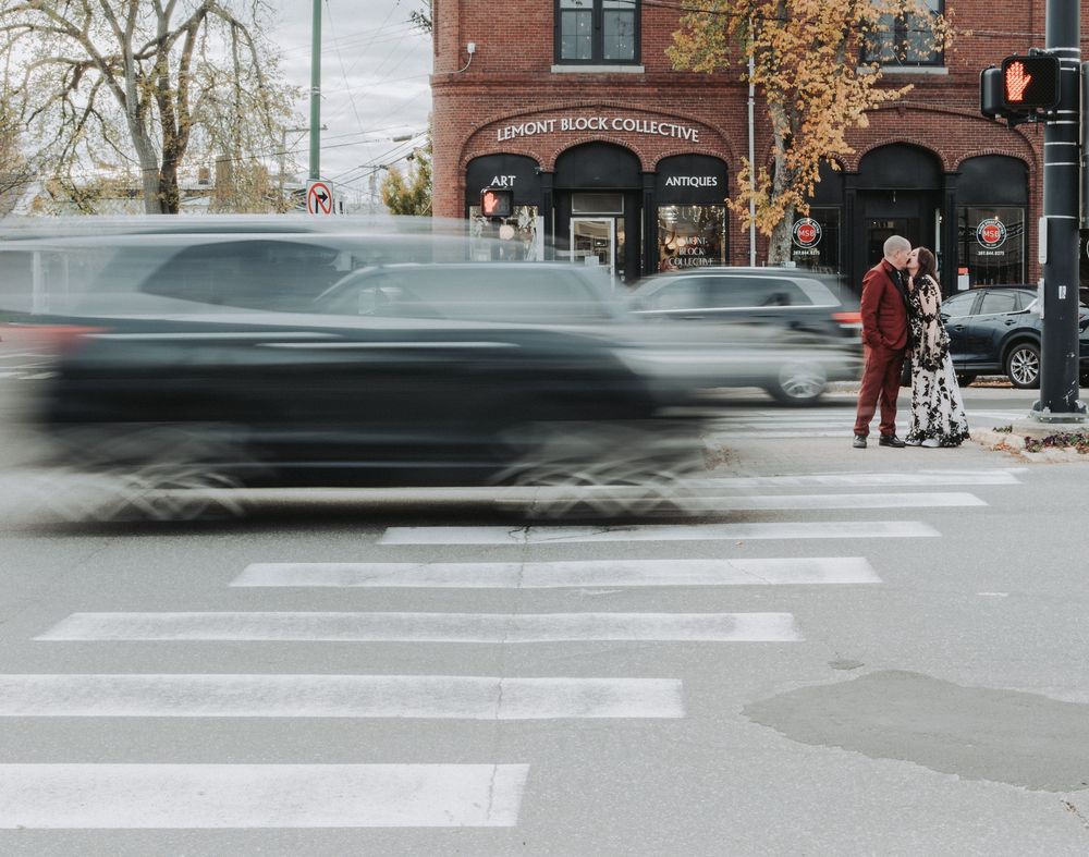 Cars speed by a bride and groom on their wedding day outside of the Lemont Hall in Brunswick, Maine.