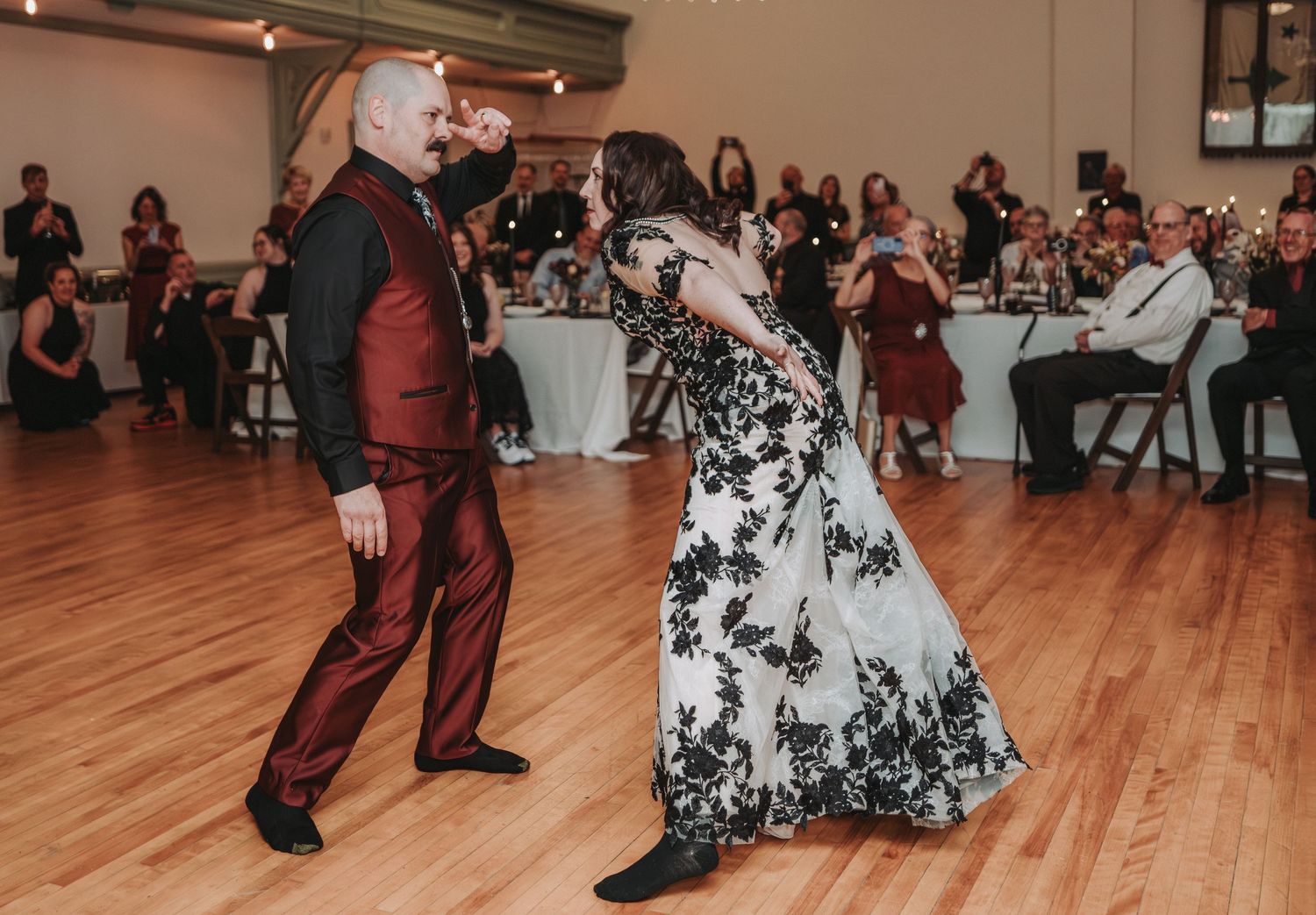 Dancers perform graceful movements on a wooden dance floor while guests watch from tables in the background.