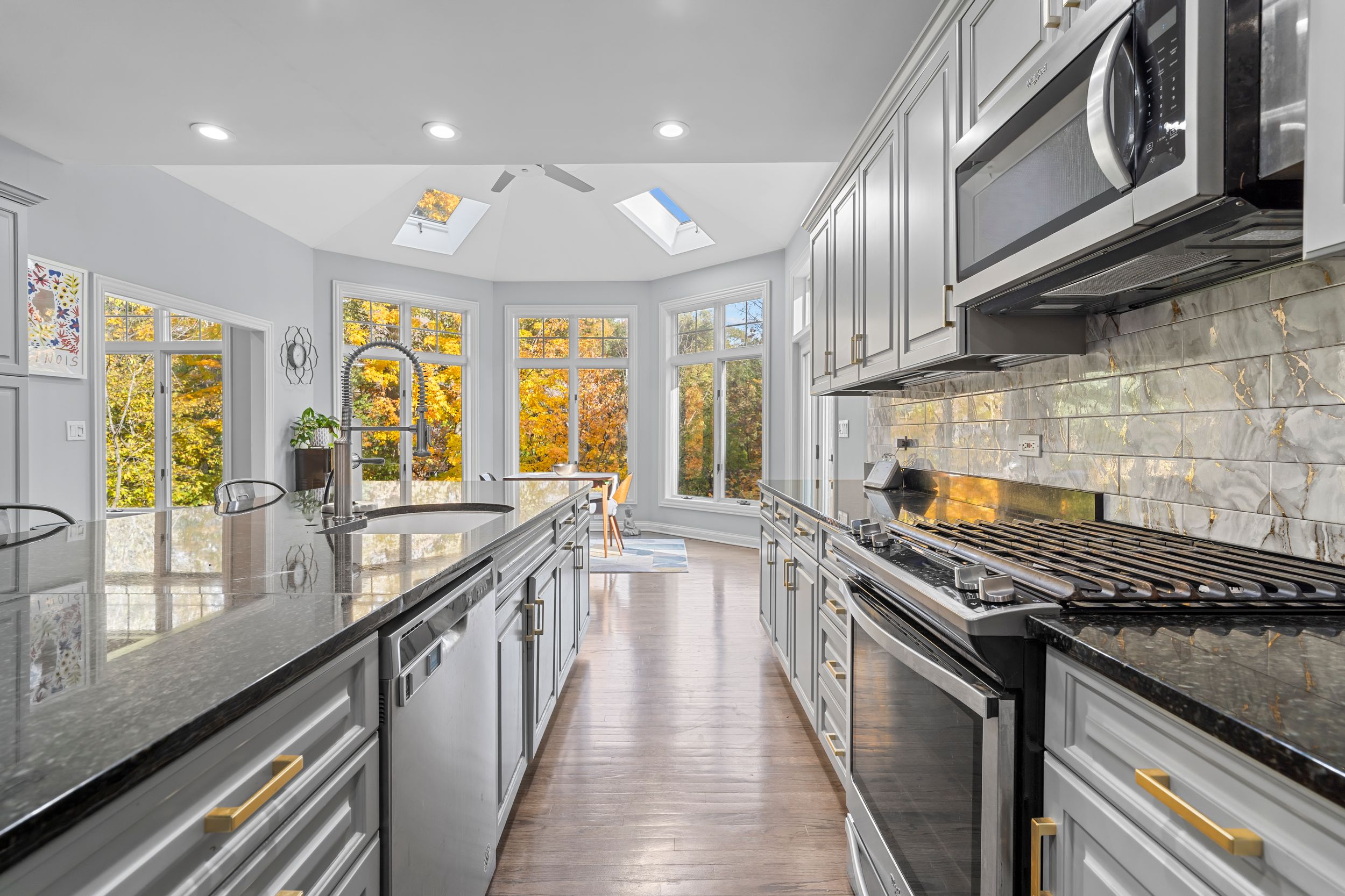 Modern white kitchen features sleek cabinetry, stone backsplash, and stainless steel appliances in an open concept design.