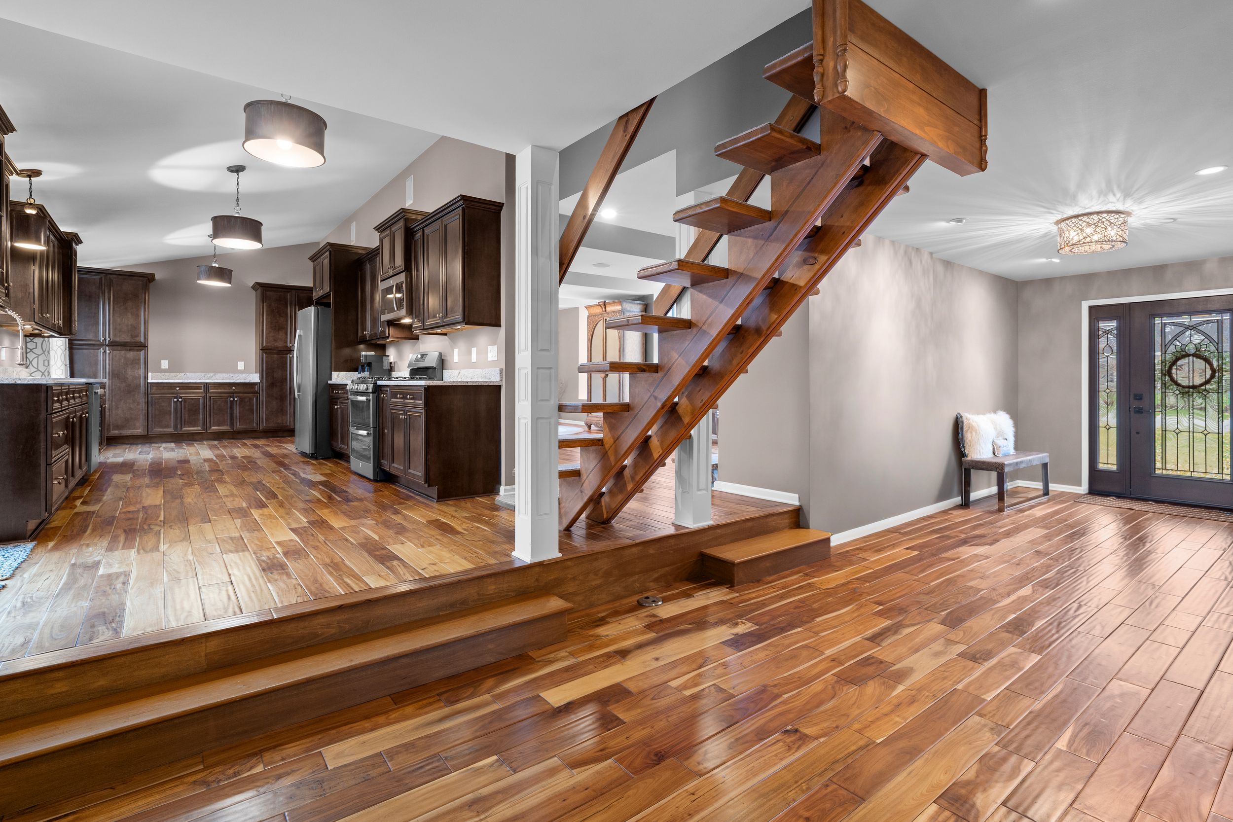 Modern open concept living space with dark wood floors, floating wooden staircase, and contemporary kitchen design.