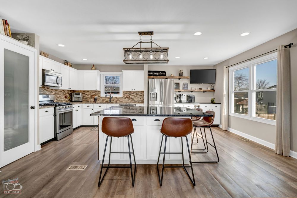Modern white kitchen featuring wood floors, center island with bar stools, and pendant lighting.