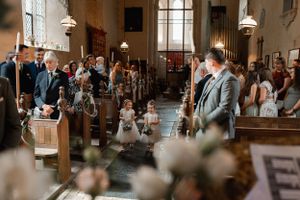 A wedding ceremony in progress inside a historic church with guests standing and watching the proceedings in a warm light atmosphere.