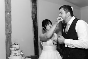 A bride and groom share cake during their wedding reception in a black and white photograph.