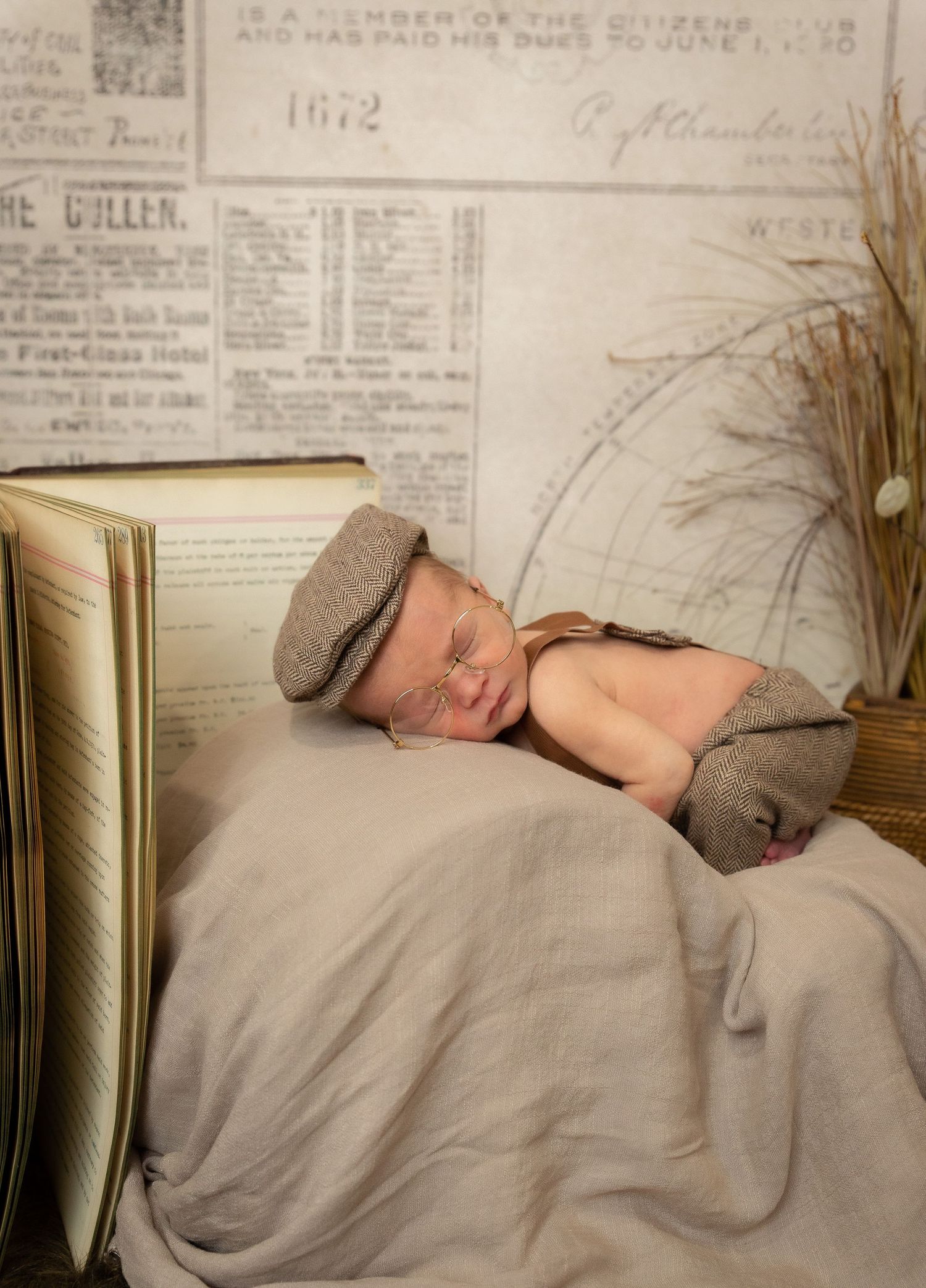 Sleeping baby on vintage backdrop with antique books and newsprint wearing a newsboy cap.