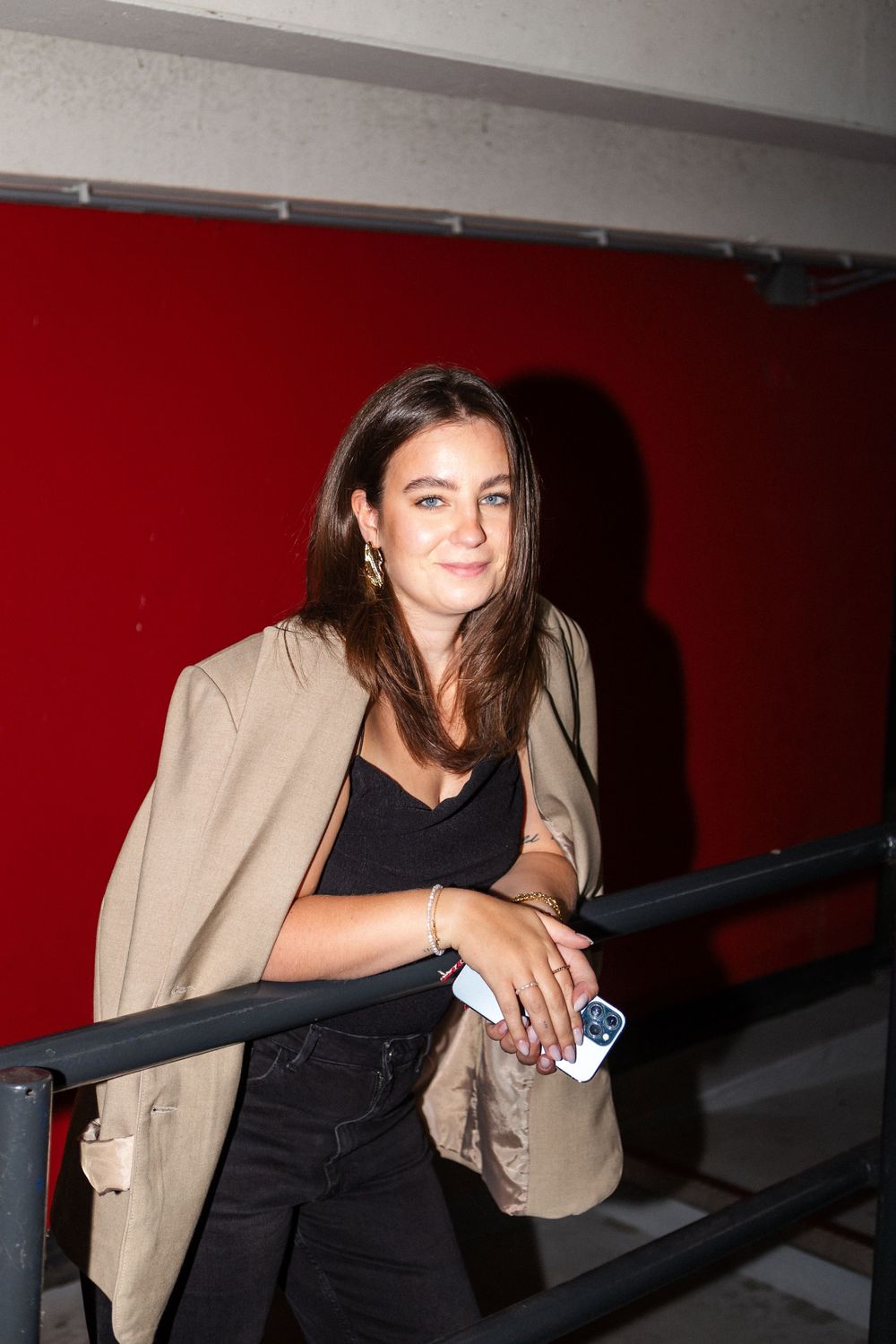 Person in casual attire standing against red wall in dimly lit setting.