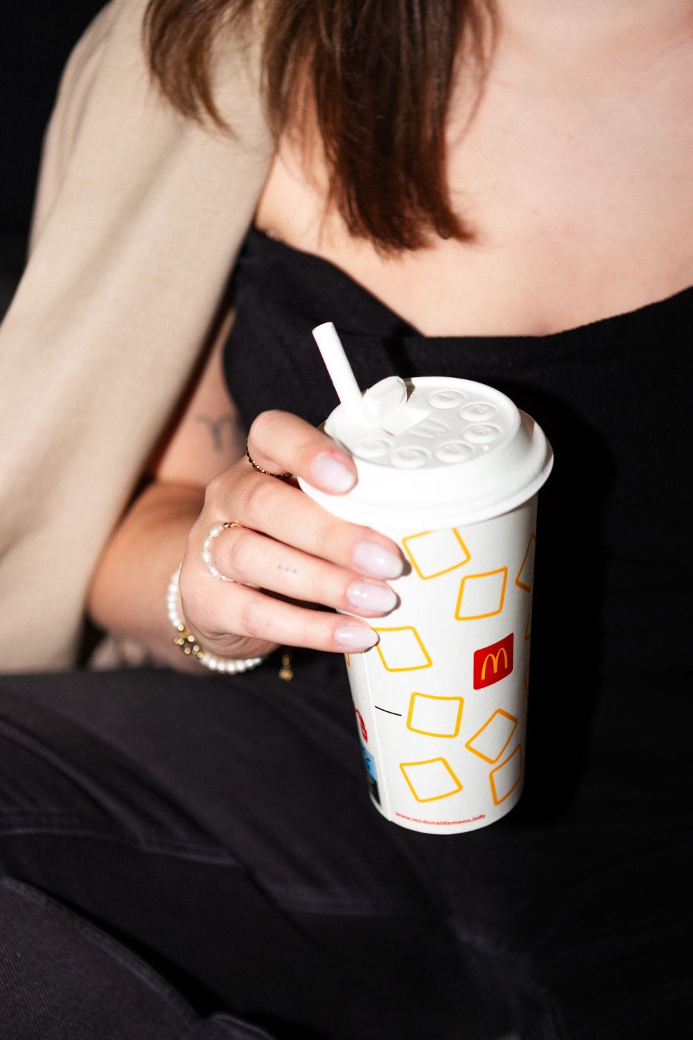 Hands holding a McDonald's beverage cup with geometric pattern design against dark clothing.