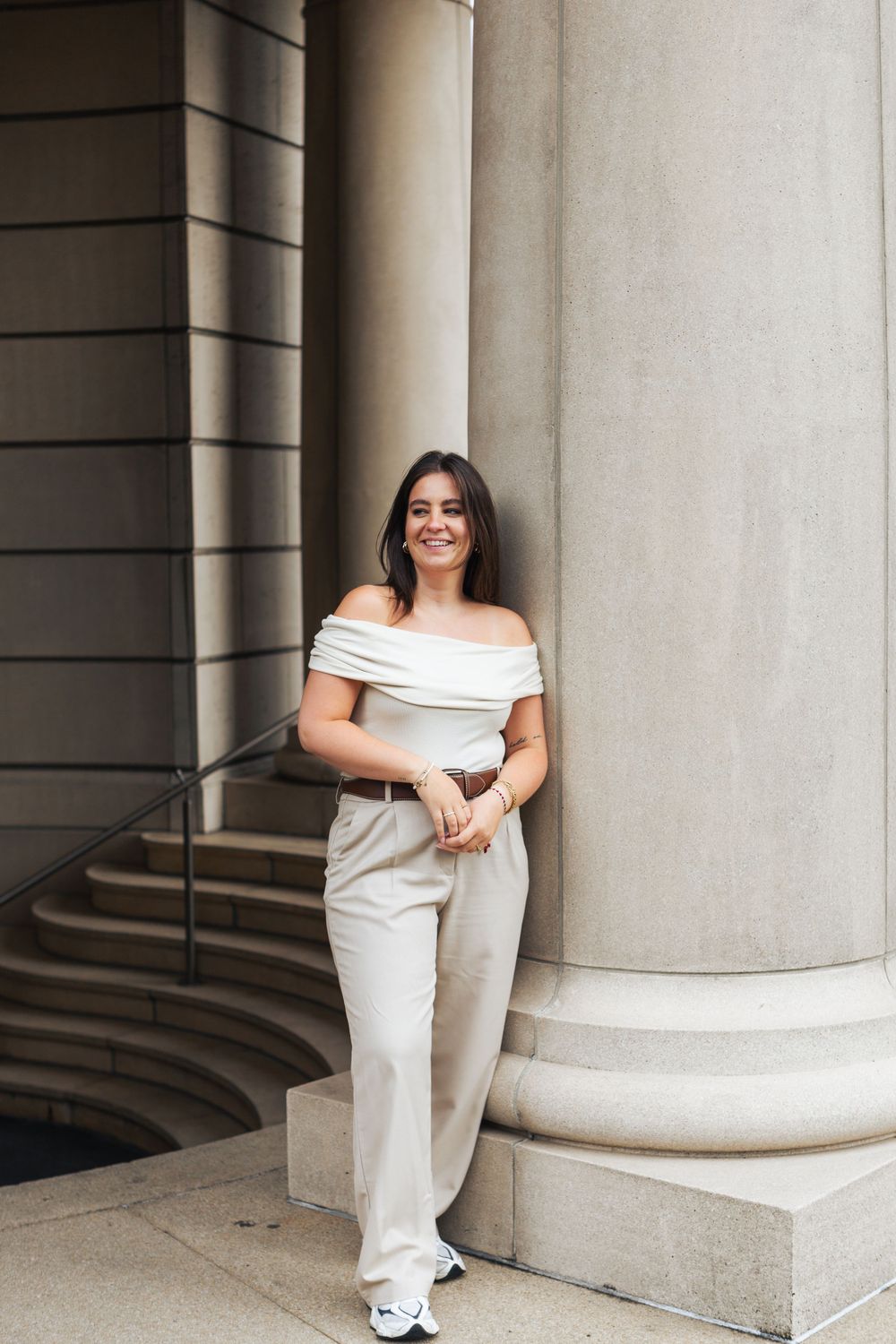 Stylish outfit featuring off-shoulder white top and light pants posed against classic column architecture.