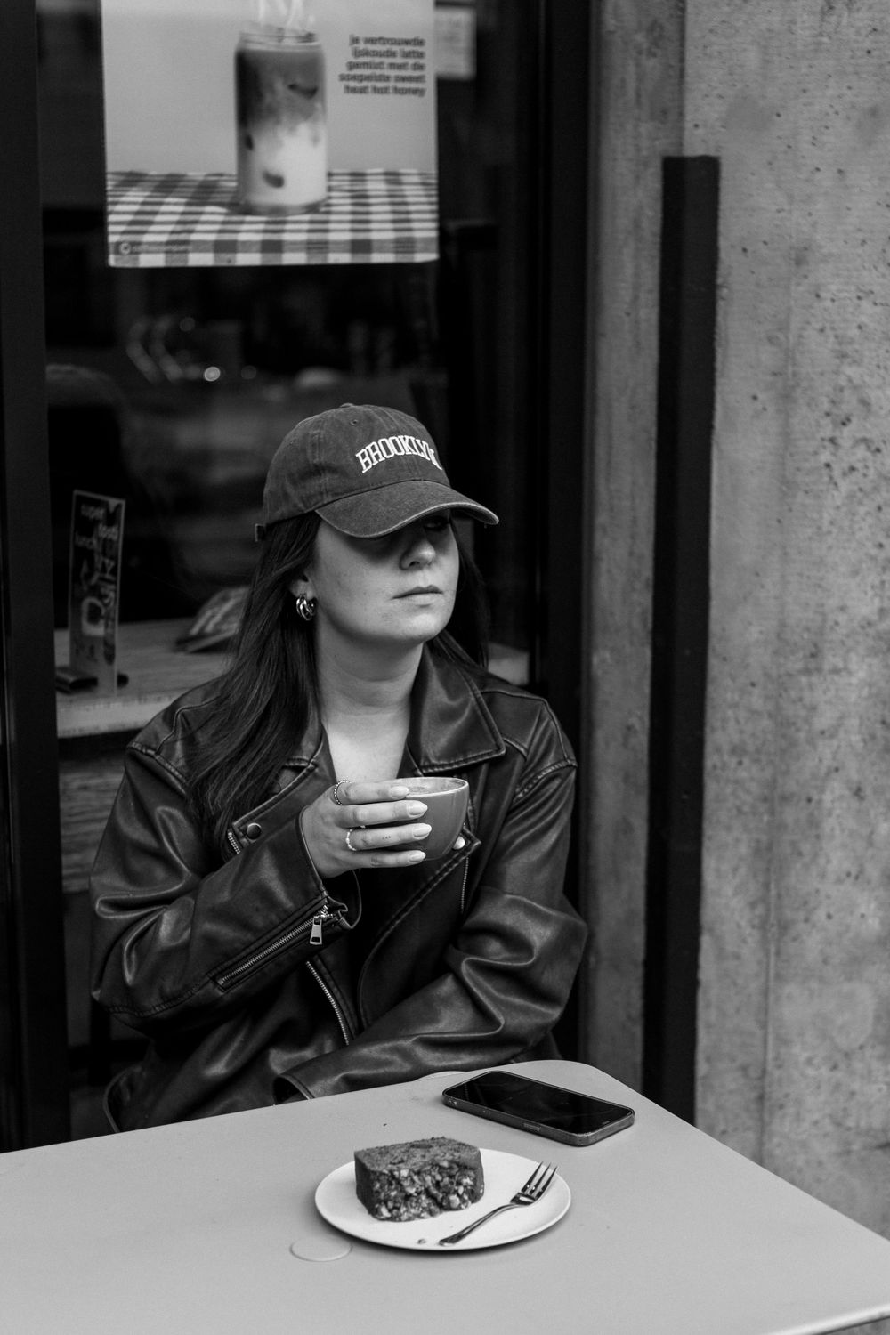 Casual cafe scene with baseball cap and leather jacket style against black and white setting.