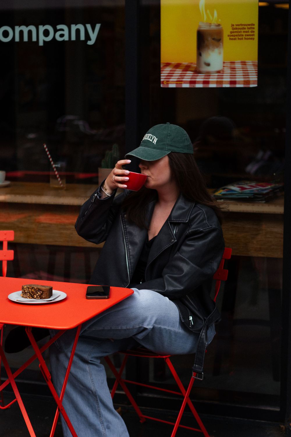 Casual cafe setting with baseball cap and leather jacket at red outdoor table.