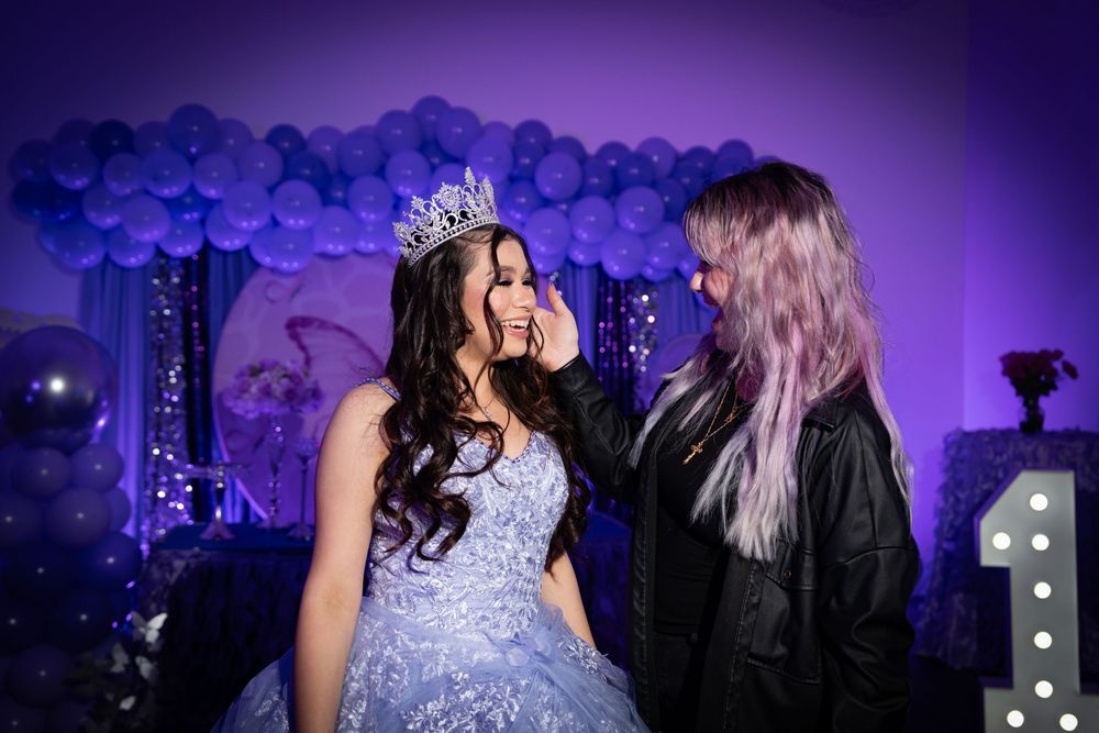 Two people share a joyful moment at a celebration with purple balloon arch and lighting effects.