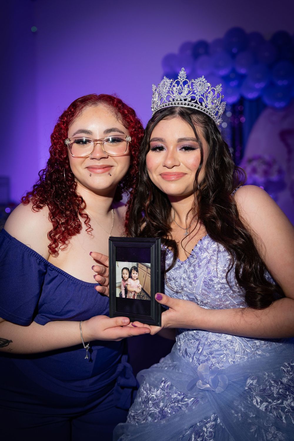 Two people in formal attire pose with a framed photo during a special celebration.