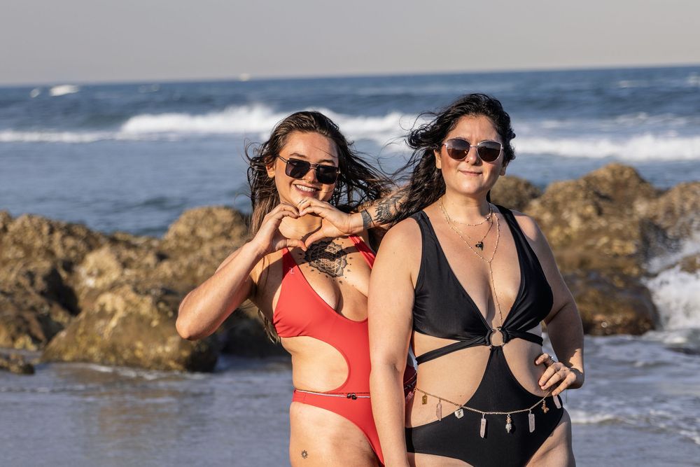 Friends enjoying a sunny beach day while sitting on coastal rocks near crashing waves.