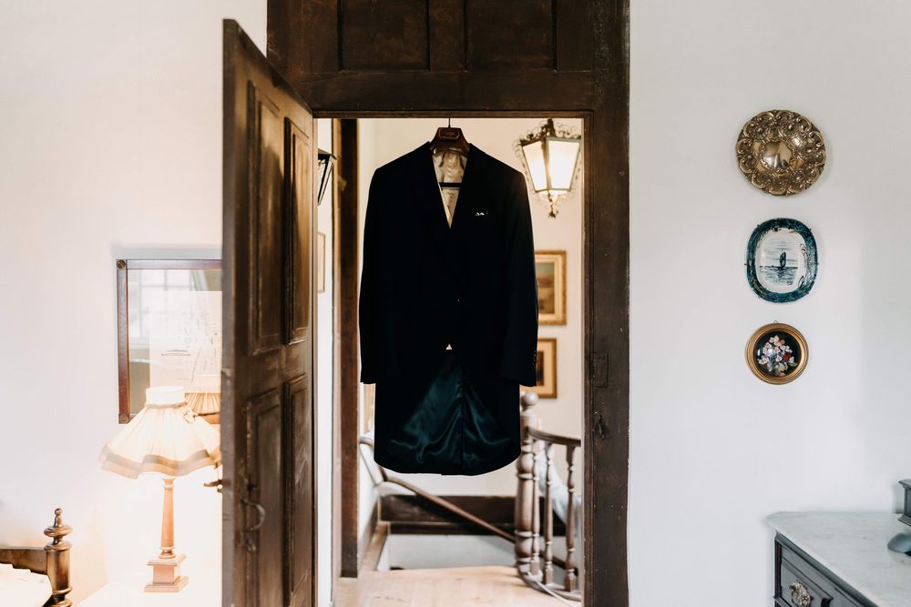 A dark suit jacket hangs in a doorway with decorative plates on the wall and a warm lamp glow in the corner.