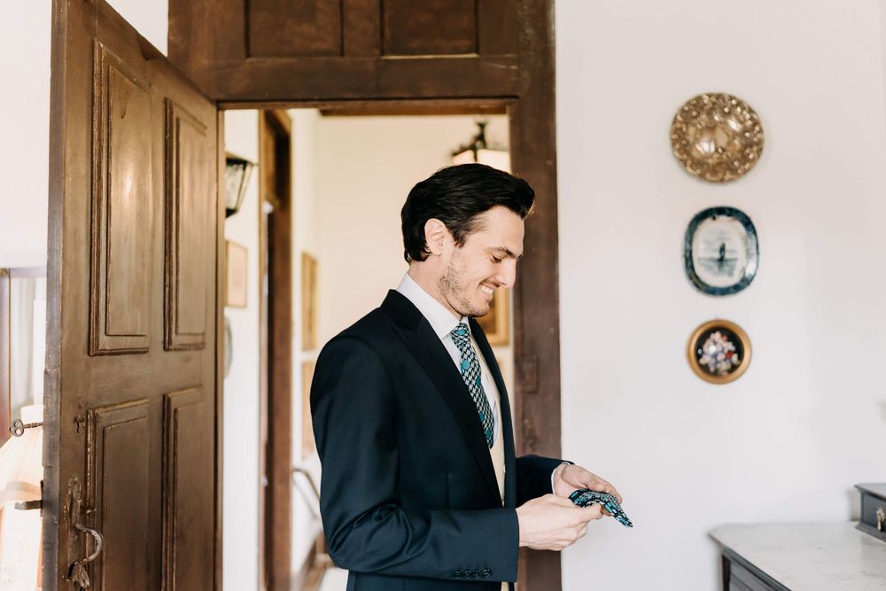 Professional in a dark suit checks his watch while standing in doorway of room with decorative plates on white wall.