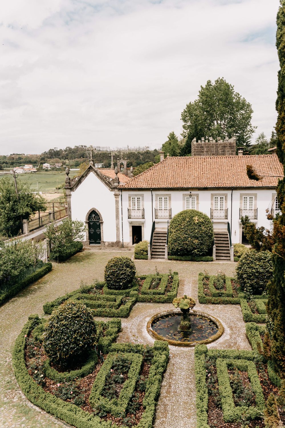 Aerial view of a Portuguese manor house with ornate formal gardens featuring geometric hedges and a central fountain.