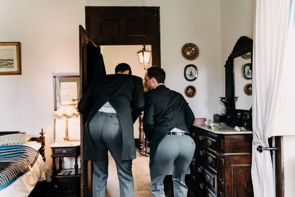 Two people wearing grey pants and black tops stand close together in a room with antique furniture.