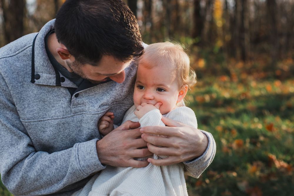 Father tenderly kissing smiling baby wrapped in white blanket outdoors.