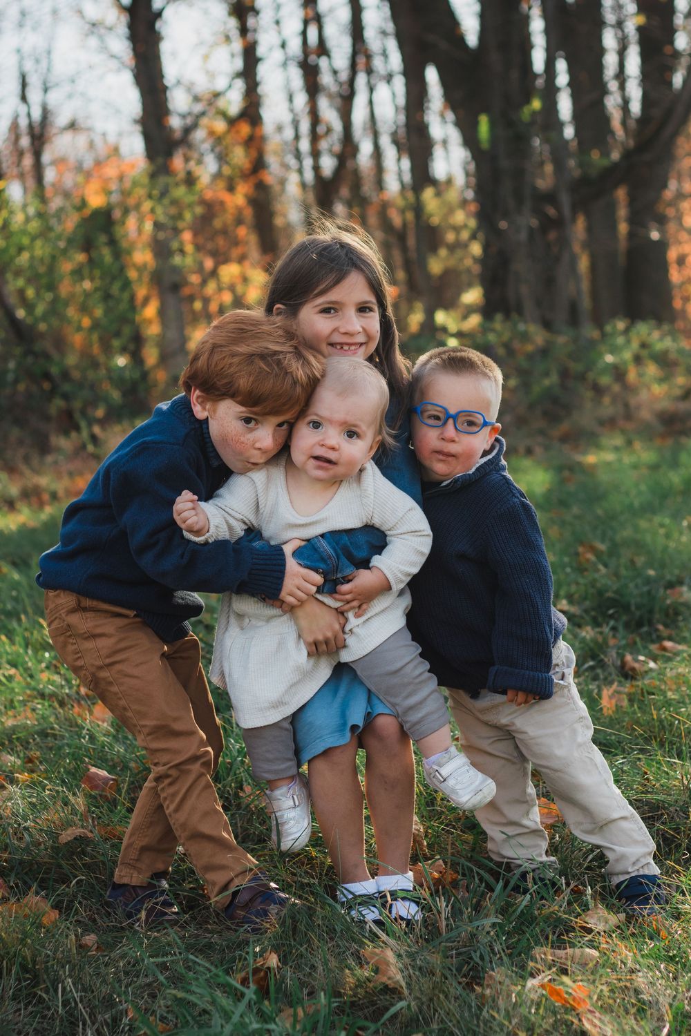Four young siblings hugging together in colorful autumn forest setting.