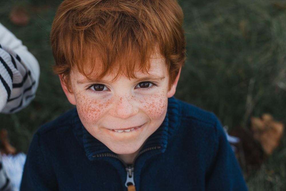 Freckled red-haired boy smiling outdoors in autumn.