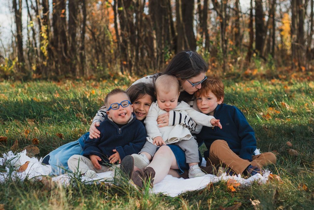 Mother hugging four young children on blanket in autumn park.