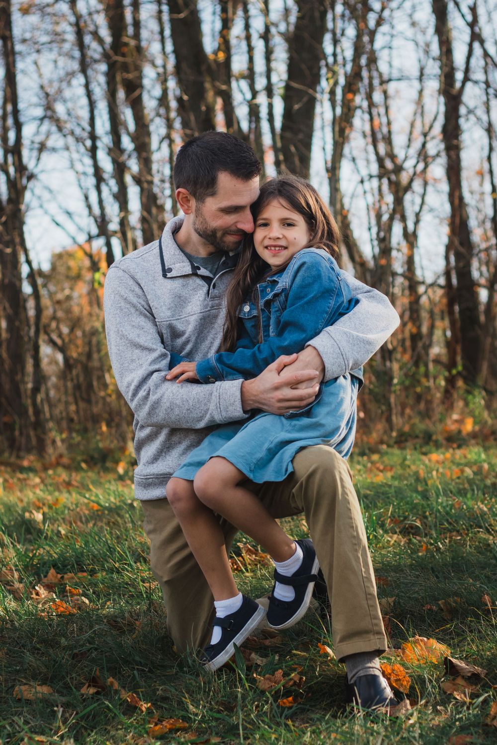 Father hugging young daughter in denim dress in autumn park.