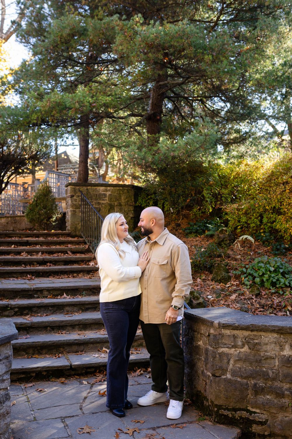 A couple shares an intimate moment on stone steps surrounded by autumn foliage and trees.