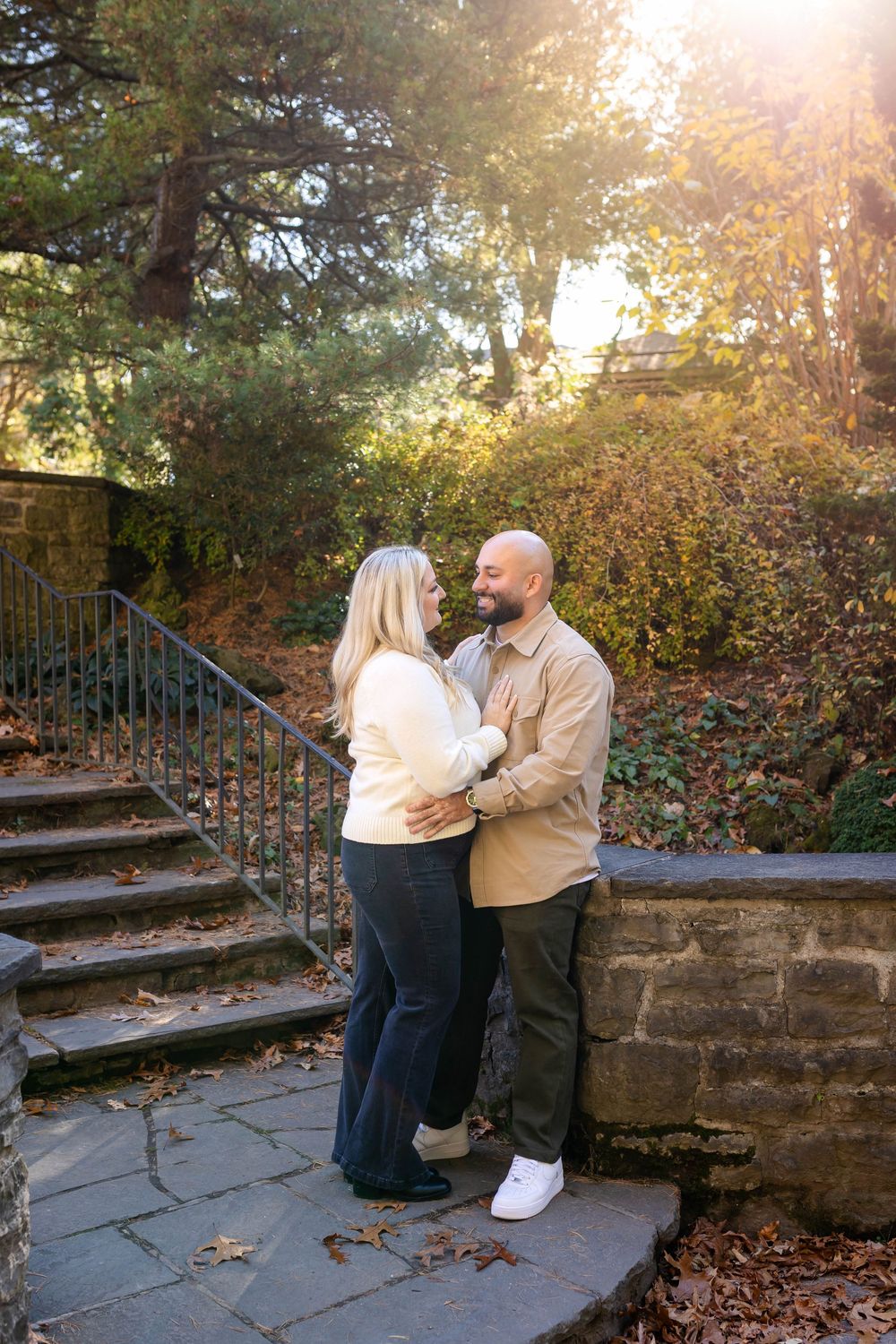 Two people embrace on outdoor stone steps with golden sunlight filtering through trees.