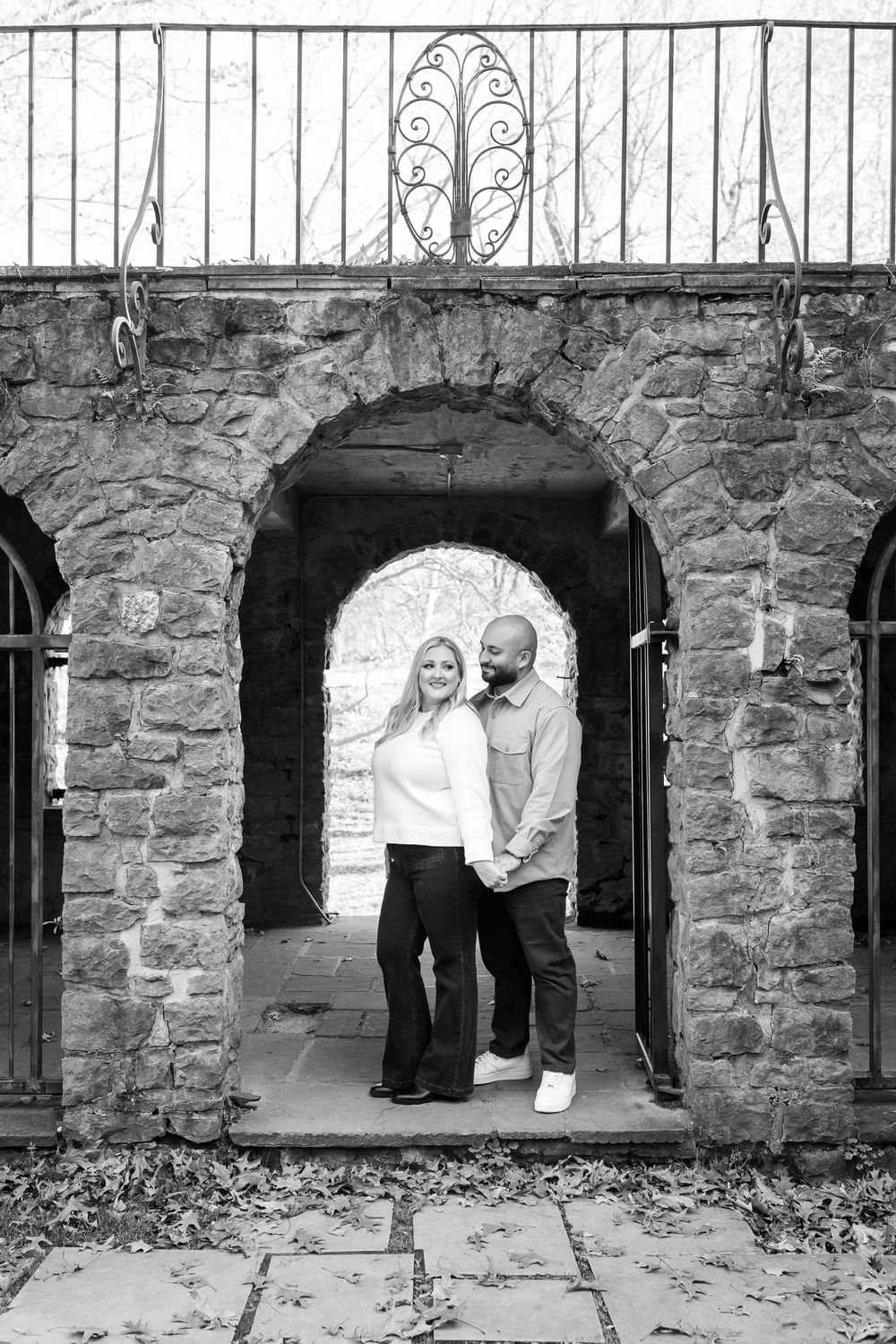 A couple stands framed within a stone archway entrance of a historic structure in black and white.