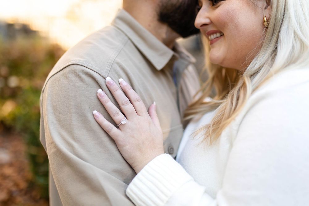 Close up of couple showing engagement ring during fall outdoor photo session with warm golden lighting.