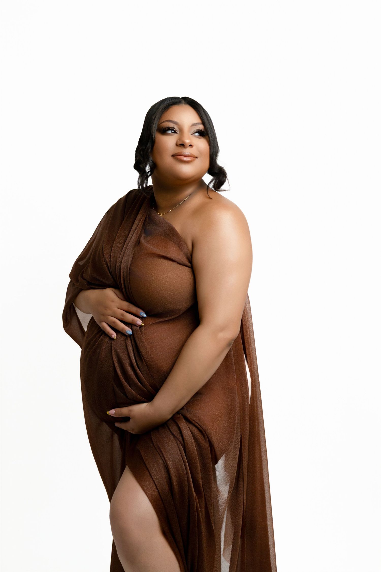 A woman with black hair smiling and looking over her shoulder towards the lighting while holding her baby bump