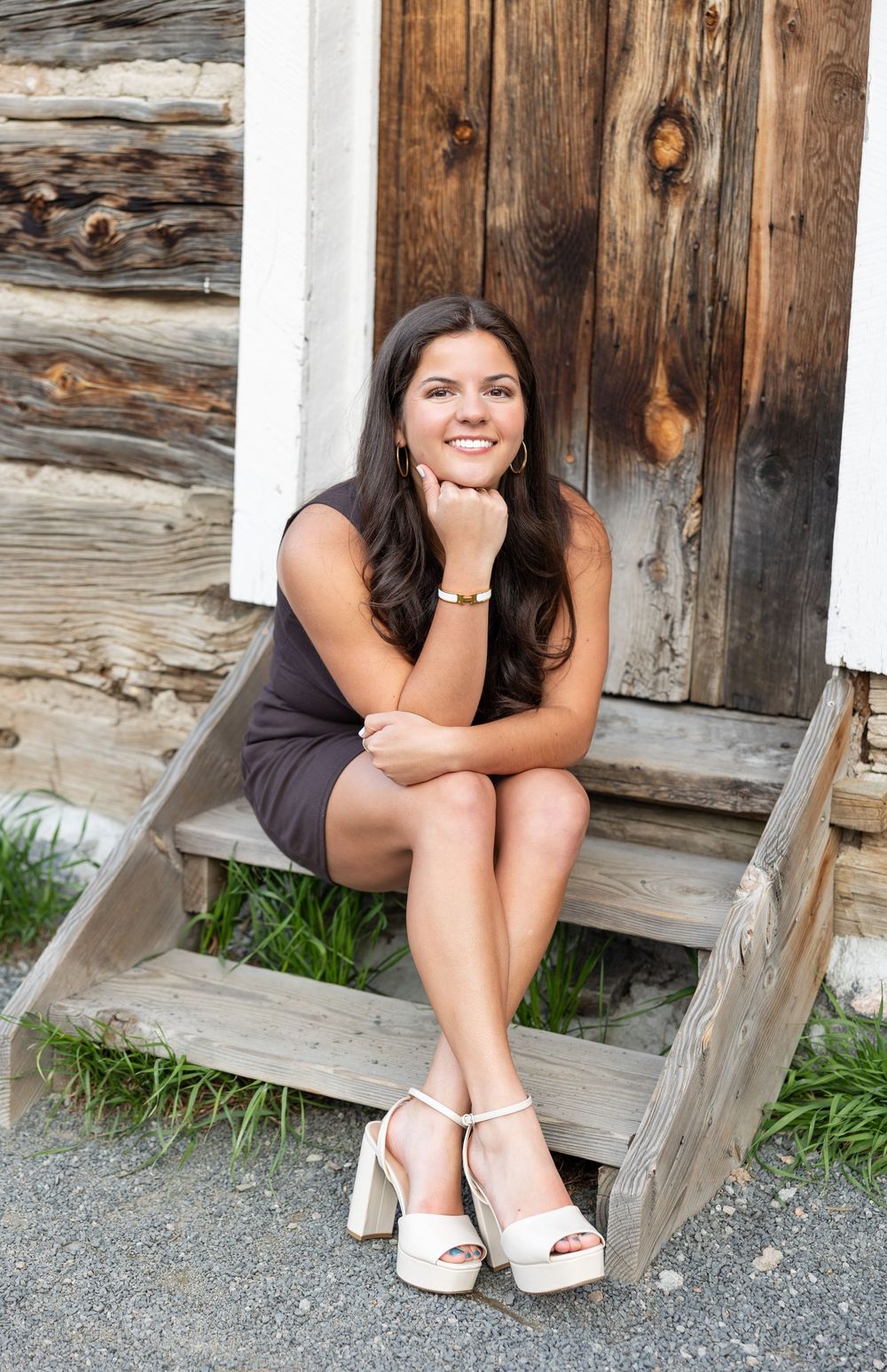 Woman in a gray dress sits on wooden steps against rustic barn door background.