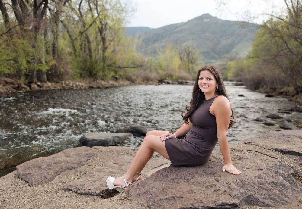 A person sits on a large rock by a flowing mountain stream surrounded by spring trees and natural scenery.