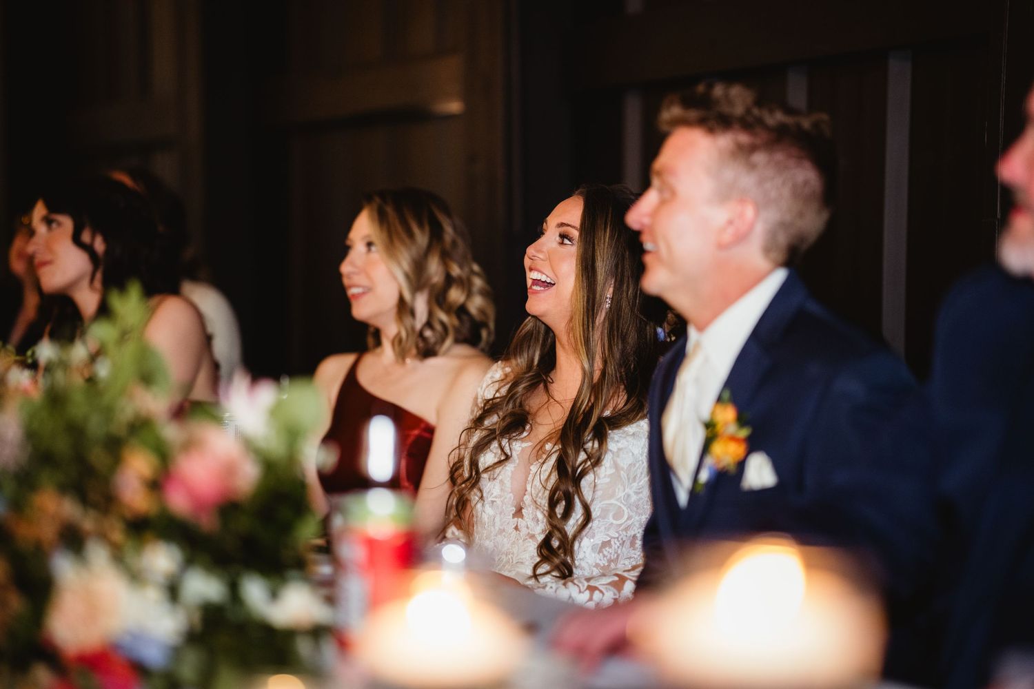 Wedding reception guests share a joyful moment while seated at a candlelit table with floral centerpieces.