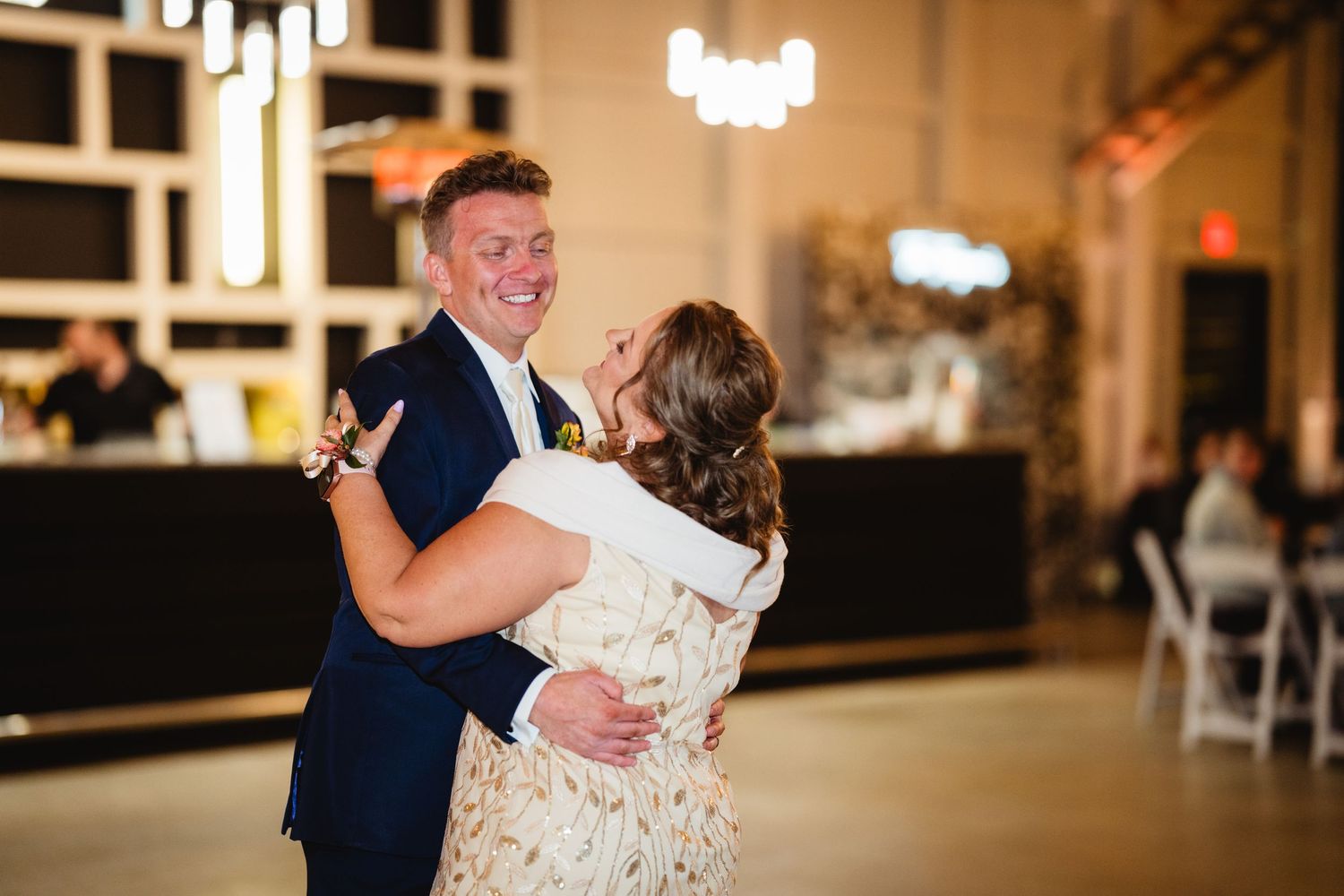 A couple shares their first dance at a wedding reception in an elegantly lit ballroom with decorative lighting.