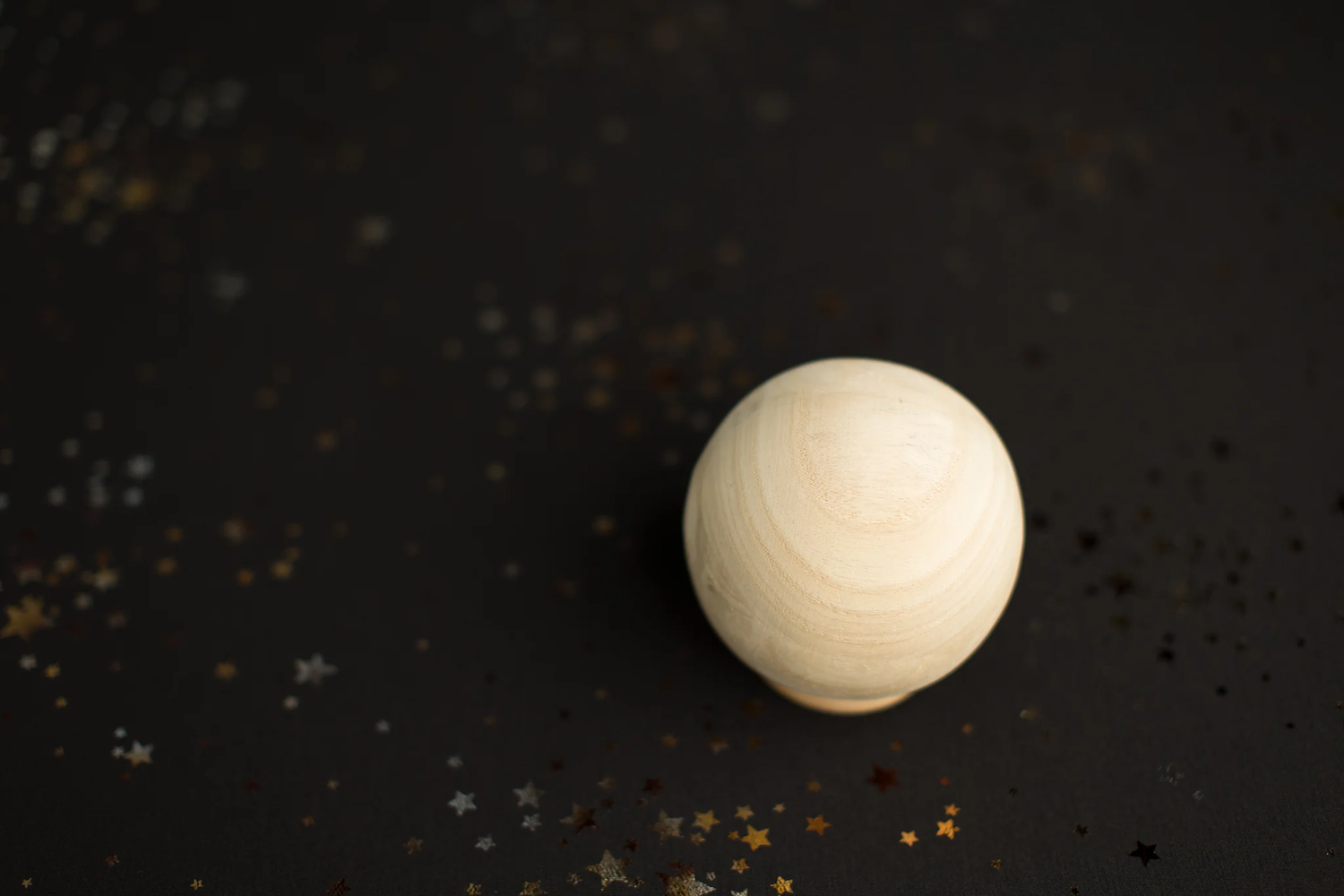 Wooden sphere on dark background with gold and silver glitter stars.